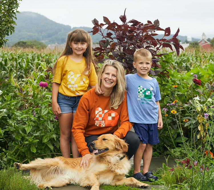 Mother and two children and golden retriever wearing cabot merch standing in front of flower garden