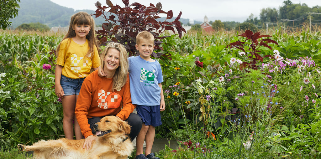 Mother and two children and golden retriever wearing cabot merch standing in front of flower garden