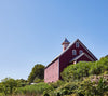 Big red barn in Vermont with a blue sky in background and green grass.