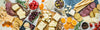 A flat lay of cheese slices, crackers, pretzels, strawberries, jams, honey, and mustard arranged on a green marble surface, creating a vibrant and appetizing spread.