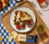 cheesy tartine lunch on a checkered table cloth with a bar of cabot cheese and pickles