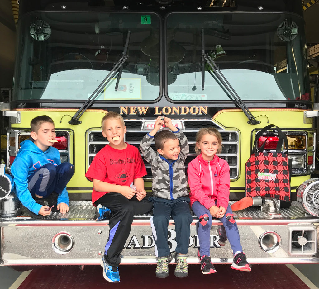 Kids sitting on the front of a fire engine after handing out samples of Cabot cheese to fire houses.