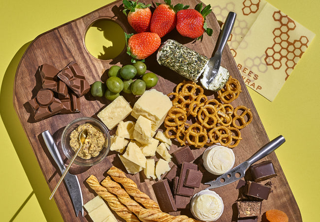 Cheese board on a yellow background featuring a variety of B Corp food items