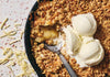 Apple crisp dessert with ice cream in a skillet with shredded cheese.