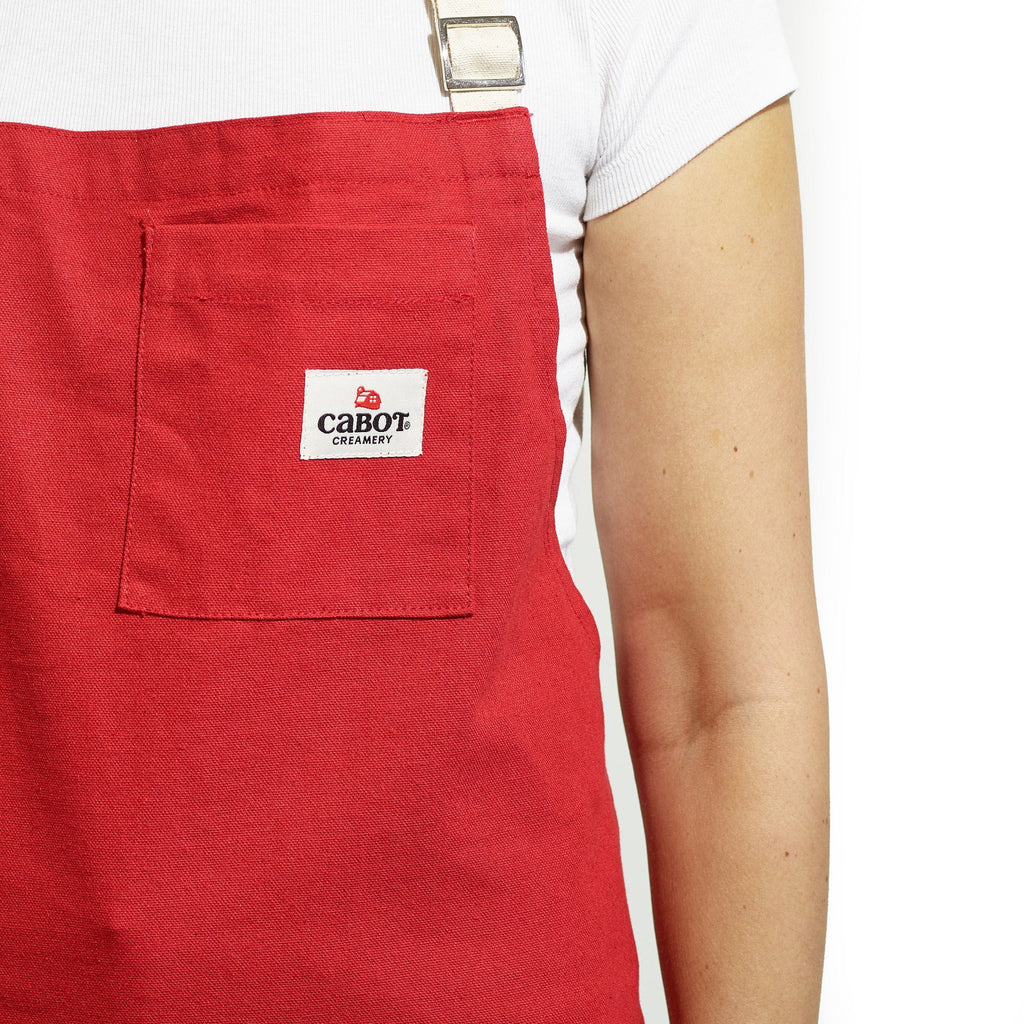 A person wears a white shirt and a plaid apron from Gallant International Inc., featuring contrast straps and a front pocket. Only the torso and part of one arm are visible.