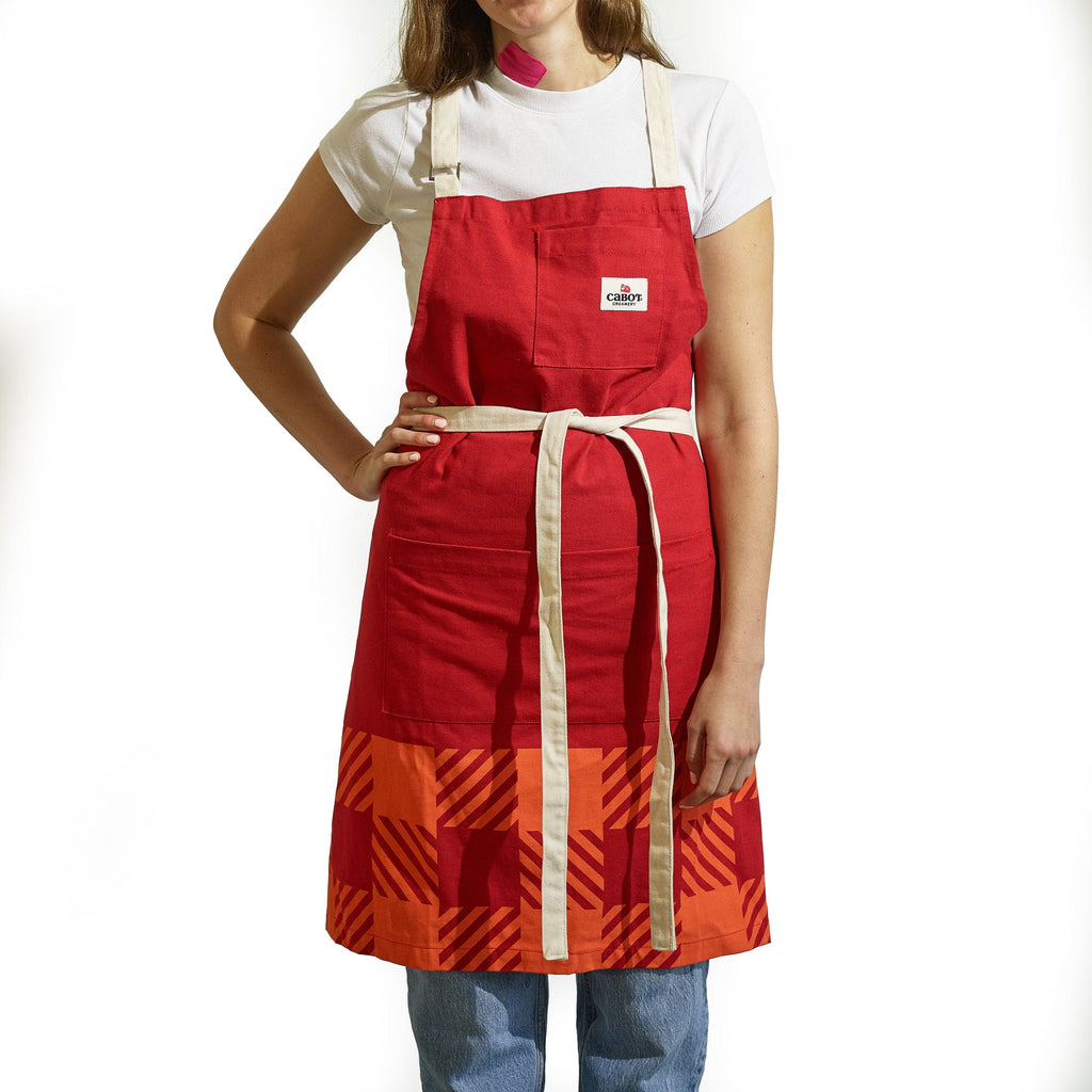 A person wearing the Gallant International Inc. Plaid Apron with beige straps, front pocket, and gear loop over a white t-shirt and blue jeans, standing against a white background.