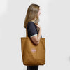 A person wears a brown canvas Where Life is Cheddar Tote featuring a pink Cabot cooperative logo.