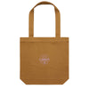 The Where Life is Cheddar Tote by Geiger Northeast is a brown canvas bag with two handles, featuring a flat bottom for convenience. At the center, it displays a circular white Cabot Creamery design that honors the heritage of the Cabot cooperative, all in a simple and minimalist style.