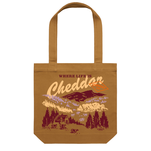 Geiger Northeast’s Where Life is Cheddar Tote is a brown Vermont-themed bag featuring the phrase “Where Life Is Cheddar” and an illustrated countryside print with cows, a barn, trees, mountains, and a sign reading Vermont—capturing the charm of Cabot cooperative country life.