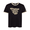 The New Duds Cheese the Day Ringer T-shirt in black and cream features beige trim on the collar and sleeves, with “Cheese the Day” printed in large, stylized beige letters on the front.