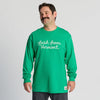 A man with a mustache wears the New Duds Fresh from Vermont Long Sleeve Chainstitched T-shirt in green, featuring white cursive text, as he stands and smiles against a plain light background.