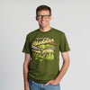 A man with glasses smiles at the camera, wearing the New Duds “Where Life is Cheddar” T-shirt featuring a colorful graphic and text. The background is plain and light grey.