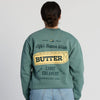 A person wearing the Life’s Better With Butter Crewneck by New Duds, featuring a green color, a butter graphic and “Life’s Better With Butter” on the back, along with Cabot Creamery, Vermont, USA.