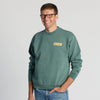 A smiling man in glasses stands against a plain light background with one hand in his pocket, wearing blue jeans and the “Life’s Better With Butter Crewneck” by New Duds.