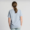 A person with brown hair in a low ponytail, wearing the New Duds Vintage Cabot Cow Graphic T-shirt and light jeans, stands facing away from the camera against a plain white background.