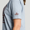 A person wearing the Vintage Cabot Cow Graphic T-shirt by New Duds in light blue, featuring the CABOT CREAMERY logo and barn graphic printed in red on the sleeve. Only their upper torso and arm are visible.
