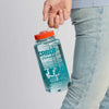 A person in light blue jeans holds the Cabot Cow Nalgene Water Bottle by Downeast Bicycle Specialists. The clear bottle, filled with water, features a red cap, blue “CABOT” branding, cow silhouettes, and measurement markings.