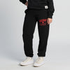 A person wearing New Duds Seriously Sharp Sweatpants in black, featuring red CHEDDAR text, paired with white sneakers and standing on a light background. Only the lower half of the body is visible.