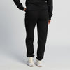 A person stands facing away, wearing New Duds Seriously Sharp Sweatpants in black, paired with a black sweatshirt and white sneakers, against a plain light background.