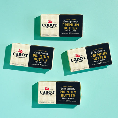 Four packages of Cabot Creamery's The World's Best Butter (4 Pack) are arranged on a light blue background, with two facing up and two facing down—showcasing the finest sea salted butter for your kitchen.