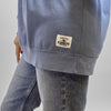 A blue heavyweight Cheddar Crewneck sweatshirt with a rectangular patch on the bottom hem that reads, Cooperative of farm families, est. 1919, Cabot Creamery.