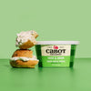 A tub of Cabot Creamery Chive & Onion Cream Cheese next to two stacked bagel halves topped with the savory cream cheese.