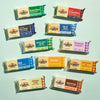 Twelve Cabot Creamery cheese blocks from the Cheese Block Party Pack, each featuring a different flavor—including Vermont Sharp Cheddar, gouda, Colby Jack, Muenster, and pepper jack—are arranged on a light green background, making this assortment an ideal gift box for any cheese lover.