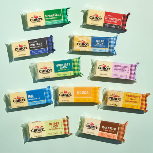 Twelve Cabot Creamery cheese blocks from the Cheese Block Party Pack, each featuring a different flavor—including Vermont Sharp Cheddar, gouda, Colby Jack, Muenster, and pepper jack—are arranged on a light green background, making this assortment an ideal gift box for any cheese lover.