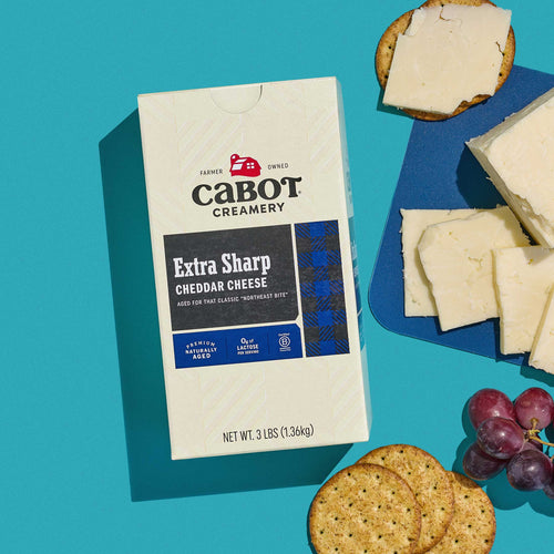 Cabot Extra Sharp Cheddar Cheese 3lb Box on blue background with grapes and crackers