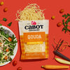 A package of Cabot Creamery Gouda Cheese sits on a red background with shredded cheese spilling out, surrounded by salad greens, grape tomatoes, a fresh plate of salad, and colorful carrots.