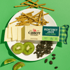 On a green background, a white plate holds Cabot Creamery Monterey Jack Cheese slices, pretzel sticks, kiwi slices, raisins, and a partially unwrapped block of Cabot Creamery Monterey Jack Cheese.