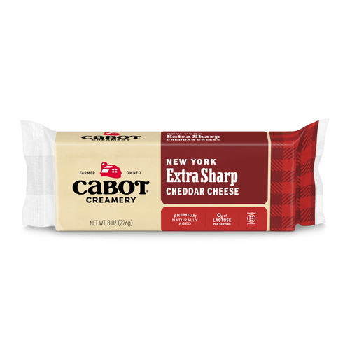 An 8 oz block of Cabot Creamery New York Extra Sharp Cheddar Cheese with a red and beige label, the Cabot logo, marked “Premium Naturally Aged sharp Cheddar” and “Lactose Free.”.