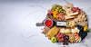 Assorted charcuterie board with cheeses, meats, fruits, and nuts on a marble surface.