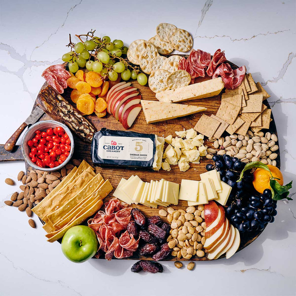 Assorted charcuterie board with meats, cheeses, fruits, and crackers on a white marble surface.