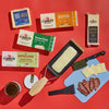 Cabot Cheeses in packaging, with meat, cheese slices, knives, jams and a raclette of melty cheese on a red background.