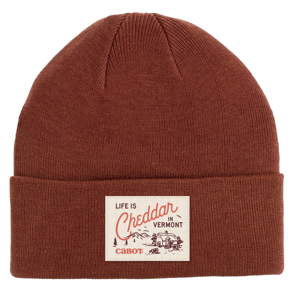 The Life is Cheddar in Vermont Patch Beanie by New Duds is a brown, recycled polyester classic cuff beanie featuring a patch with Life is Cheddar in Vermont above barns and Cabot for cozy, sustainable style.