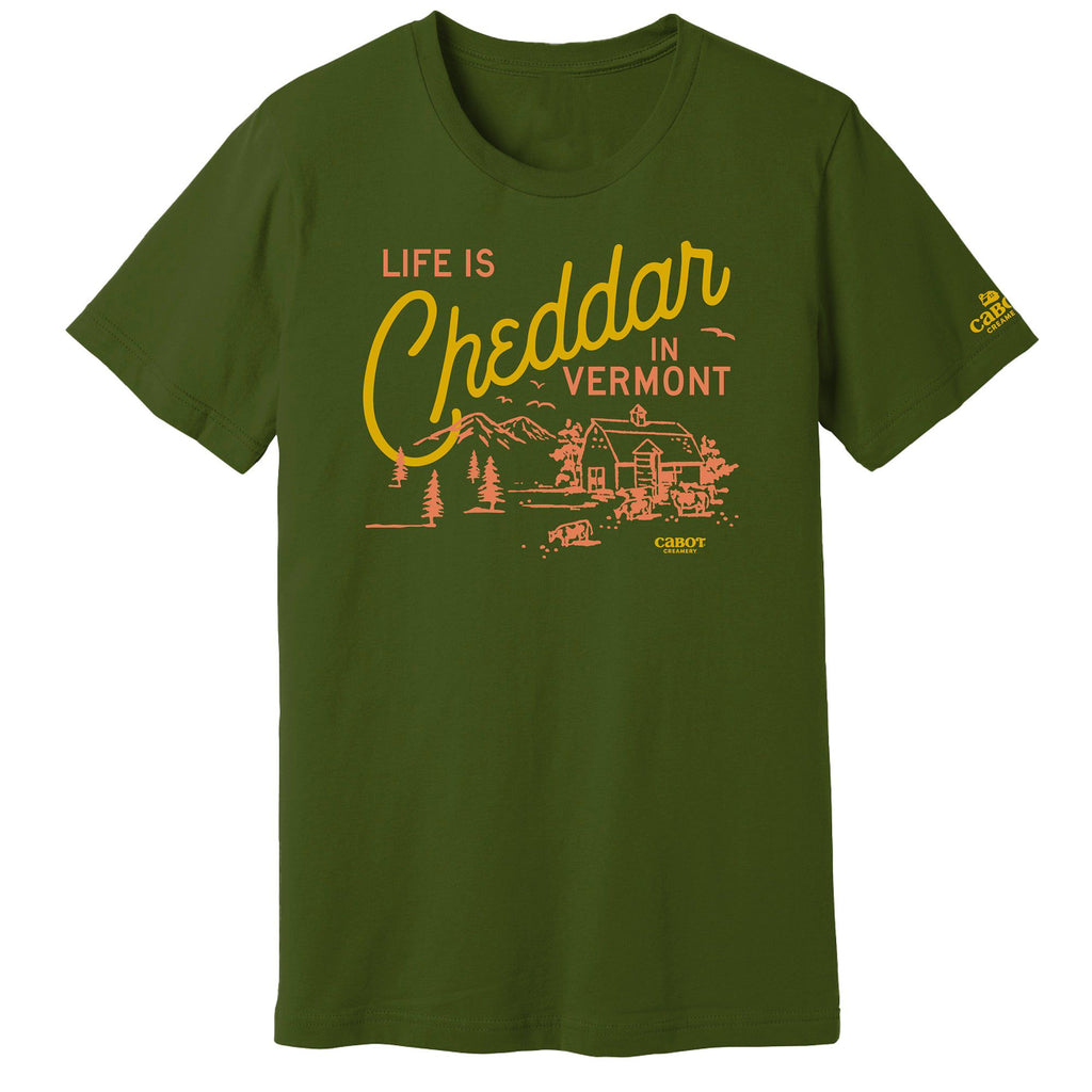 The New Duds Life is Cheddar in Vermont T-shirt features a green color with a yellow and orange rustic farm graphic. Cheddar appears in large script, while the rest of the phrase is in bold uppercase letters.