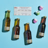 The Vermont Sugarhouse Sampler includes four small bottles of pure maple syrup labeled by flavor intensity, a tasting guide card, and three small patterned paper baking cups arranged on a blue surface.