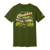 The Where Life is Cheddar T-shirt by New Duds features an olive green color and showcases a graphic of scenic mountains, a cabin, pine trees, cows, and a red sign. The design includes the text “WHERE LIFE IS Cheddar VERMONT” and “CABOT.”.