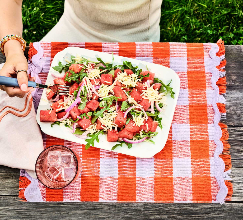 Eating a Watermelon, shredded cheddar cheese, arugula salad on wooden table with Cabot Shredded Cheese packaging.