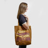 A person carries a brown canvas Where Life is Cheddar Tote featuring a scenic print of cows and the text Where life is Cheddar and Vermont USA.