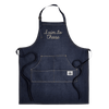 The New Duds I Aim To Cheese Apron features dark blue denim with white stitching, front pockets, and “I Aim To Cheese” embroidered in cursive across the chest. It includes black neck and waist straps for a comfortable fit.