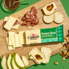 Cabot Sharp Cheddar Cheese on a cutting board with crackers and nuts, apples and salami with green background