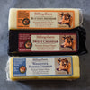 Three blocks of Vermont artisan cheddar cheese from Billings Farm: Butter Cheddar in yellow wrapping, Sweet Cheddar in red wrapping, and Woodstock Reserve Cheddar in blue wrapping. Each has a cow illustration on the label.