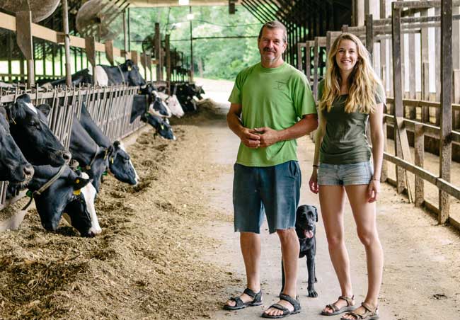 two cabot farmers in a barn with holstein cows