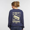 A person with light brown hair in a ponytail wears the New Duds Butter Long Sleeve T-shirt—a navy heavyweight cotton shirt featuring yellow It doesn’t get any butter than Vermont text and a butter illustration.
