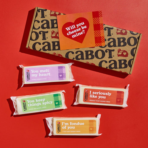 The Cabot Creamery Life Is Cheddar With You Gift Box features award-winning cheeses behind four playful cheese blocks with messages: You melt my heart, You keep things spicy, I seriously like you, and I’m fondue of you.