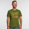 A man with short brown hair and a beard smiles in the New Duds Life is Cheddar in Vermont T-shirt, made of ring-spun cotton and featuring yellow text over a rustic farm scene with mountains, trees, cows, and a barn.