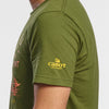 A person wears the New Duds Life is Cheddar in Vermont tee, featuring a green color and sleeve printed with Cabot Creamery and a cow logo in yellow. Only the upper body and part of the arm are shown against a plain background. Made from soft ring-spun cotton.