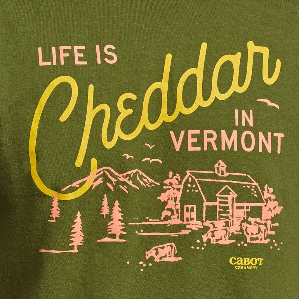 The Life is Cheddar in Vermont T-shirt by New Duds features yellow and pink text with a rustic farm scene—mountains, trees, cows, barn, and Cabot Creamery logo—crafted from soft ring-spun cotton for comfort.